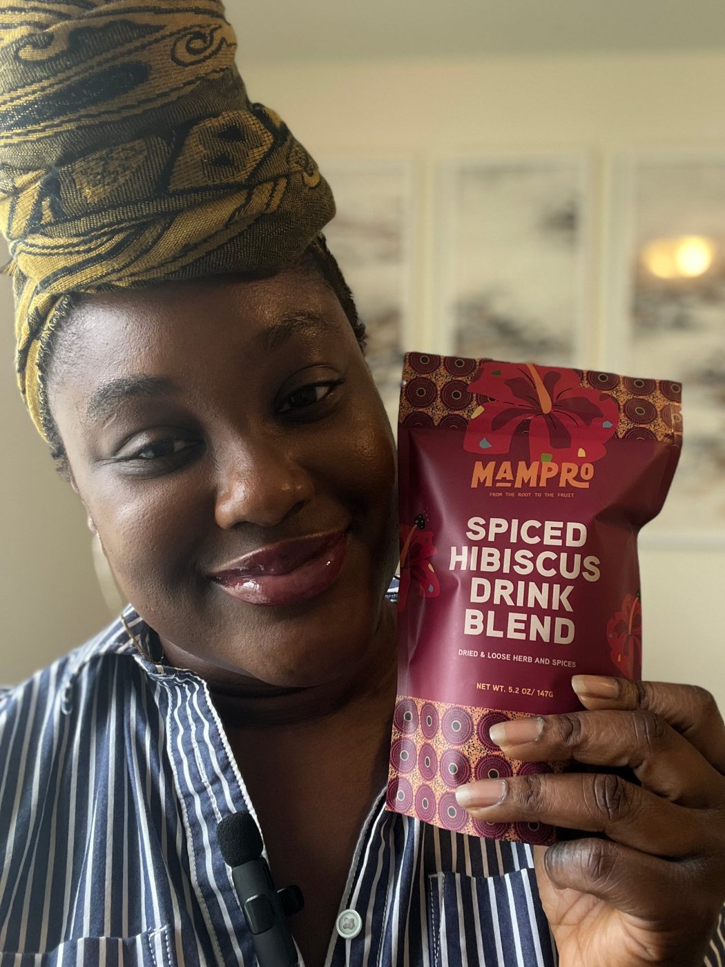 Smiling woman in a headwrap holding a pouch of Mampro Spiced Hibiscus Drink Blend